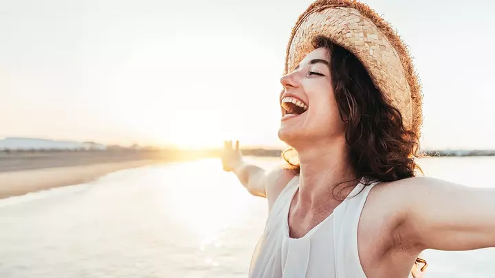 A happy middle-aged woman with outstretched arms on a beach in sunset